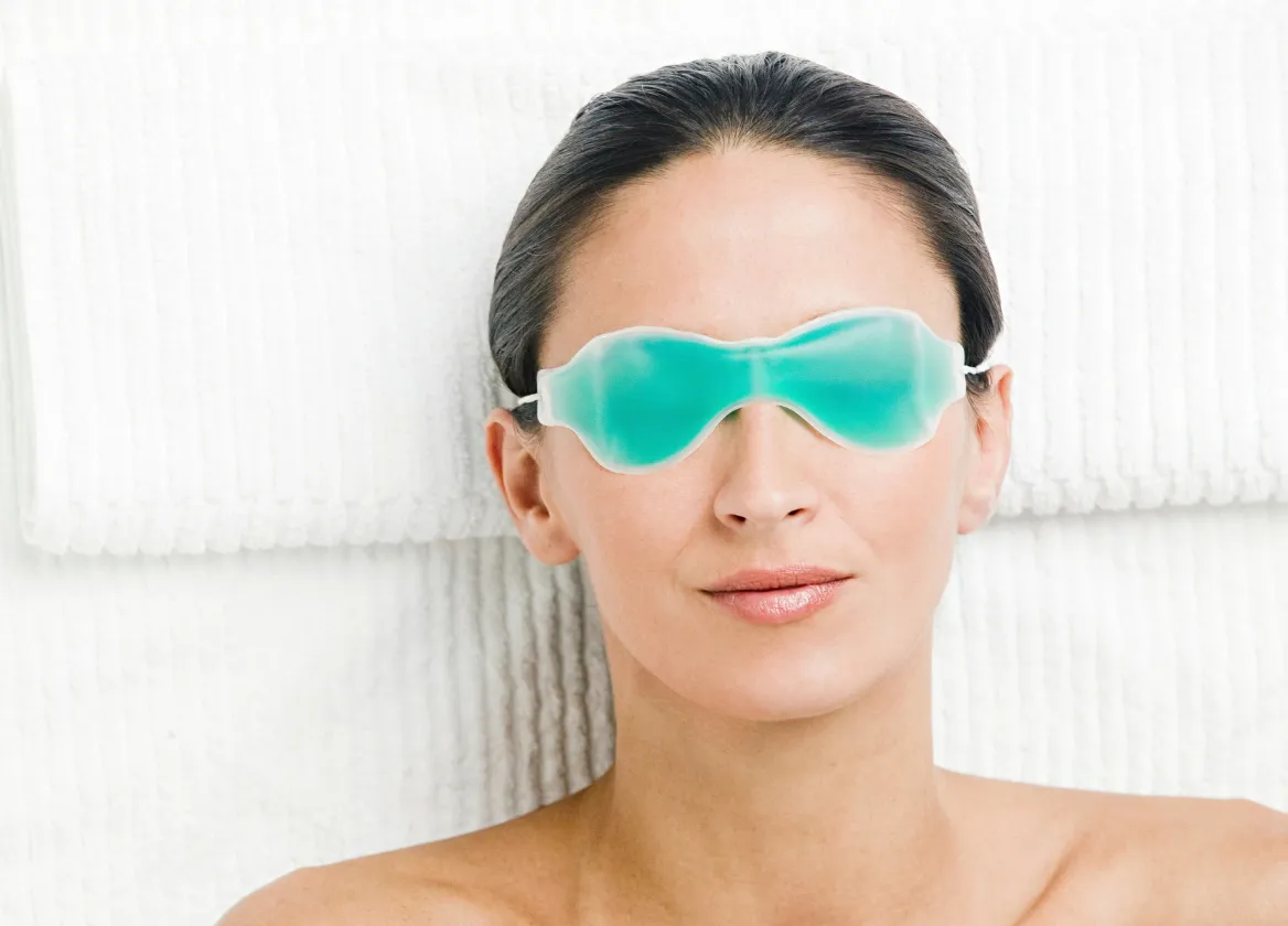 Mujer recostada con un antifaz de gel frío en los ojos, uno de los cuidados del postoperatorio de la blefaroplastia